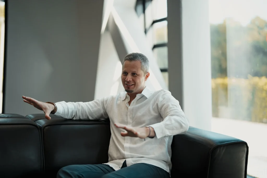 Max Simon sitzt auf einem Sofa, die Arme geöffnet, mitten im Gespräch
